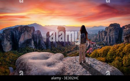 A hiker woman stands on a rock and looks at a beautiful sunset beahind the Meteora valley mountains, Kalabaka, Greece Stock Photo
