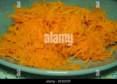 A heap of freshly shredded bright orange carrots on a ceramic plate. High-angle view, focus on texture. Concept of healthy eating, cooking ingredients, and organic vegan food. grated carrots on a plate, close-up. High quality photo Stock Photo