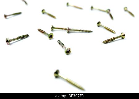 Scattered yellow zinc wood screws on white background, shallow depth of field. Professional fasteners for woodworking and home renovation. Stock Photo