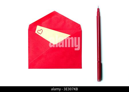 An open red envelope reveals a small beige card with a hand-drawn red heart, placed next to a red felt-tip pen. This vertical, minimalist flat lay is Stock Photo