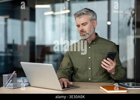 Experienced man multi-tasking and communicating using modern digital technology while managing tasks at a corporate workplace, representing productivity and work-life balance Stock Photo