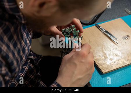 A person carefully handles a small electronic circuit board, meticulously assembling or repairing it with focused attention. Stock Photo