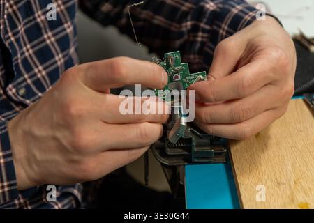 A person carefully handles a small electronic circuit board, meticulously assembling or repairing it with focused attention. Stock Photo