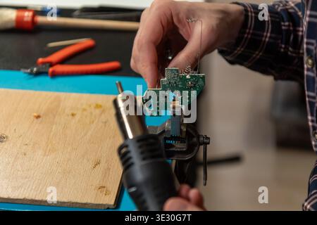 This high-angle close-up shot captures an electronics technician or engineer intently focused on repairing a small green printed circuit board. Using Stock Photo
