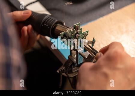 This high-angle close-up shot captures an electronics technician or engineer intently focused on repairing a small green printed circuit board. Using Stock Photo