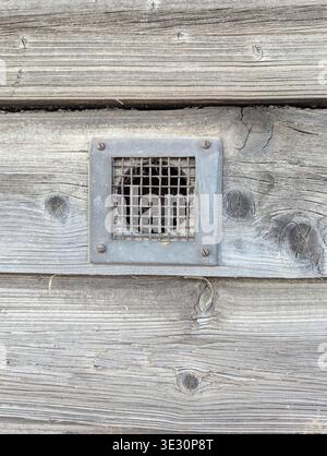 Metal Vent Grille On Wooden Siding, Closeup Of Square Vent Framed By Aged Gray Planks, Protective Mesh And Visible Screws, Subtle Rust Stains And Geom Stock Photo
