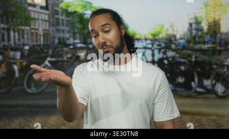 Man extending open palm hand forward on street beside canal and parked bicycles; skepticism doubt questioning. Stock Photo