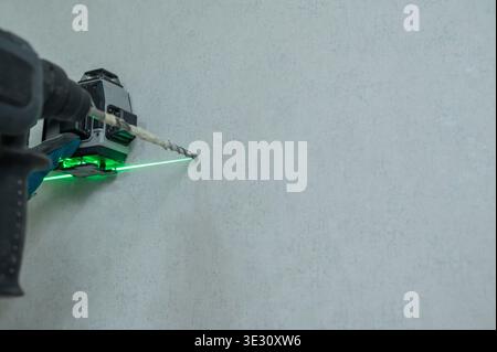 A man measures distances with a laser level and drills into a wall with a hammer drill. Stock Photo