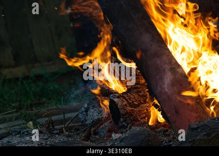 A roaring log campfire crackles with intense heat, surrounded by the rustic ambiance of an old oil drum. Perfect for evoking themes of outdoor parties Stock Photo