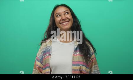 Woman wearing glasses and patterned shirt smiling with closed eyes showing teeth in green studio; joyful confidence warmth. Stock Photo