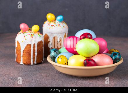 Easter cakes decorated with colorful eggs and plate with multicolored eggs on brown background Stock Photo