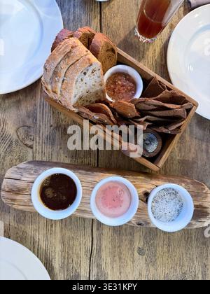 Wooden box with rye bread slices, bread chips and dipping sauces arranged on table in restaurant setting, rustic appetizer serving with natural Stock Photo