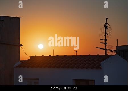 Sunset over Mediterranean rooftop with satellite dishes and antenna towers silhouetted against golden sky Stock Photo