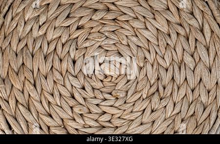 Close-up of a tightly woven natural fiber surface arranged in a circular spiral pattern. The organic texture features warm beige and tan tones with vi Stock Photo