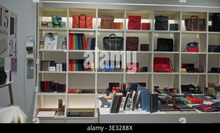 Blurred retail display wall of bags, notebooks and boxes with shallow bokeh and soft defocused shelving in a shop; background backplate copyspace calm Stock Photo
