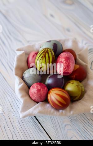 Naturally dyed Easter eggs in vivid multiple colors — red, green-yellow, grey-blue, burgundy — with botanical impressions, in a linen cloth bowl. Whit Stock Photo