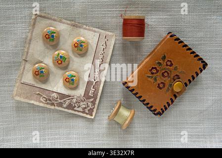 Sewing Button Kit. Card of wooden vintage buttons with raised painted flower design and matching cotton on wooden reels and old embosed leather needle Stock Photo