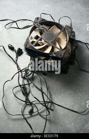 pile of dusty black plastic computer cooling fans with tangled wires and frames, top view on grey textured surface, electronic hardware waste Stock Photo