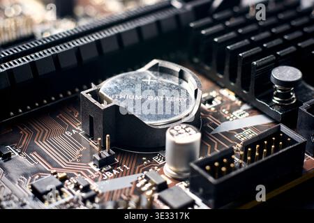 silver lithium battery in black plastic holder on computer motherboard, detailed electronic circuits and capacitors, macro view with soft focus Stock Photo