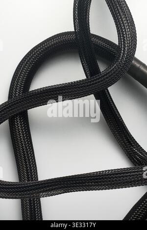 black braided nylon power cables with mesh sleeves, dark textured synthetic material, soft focus on gray background, cable organization concept Stock Photo