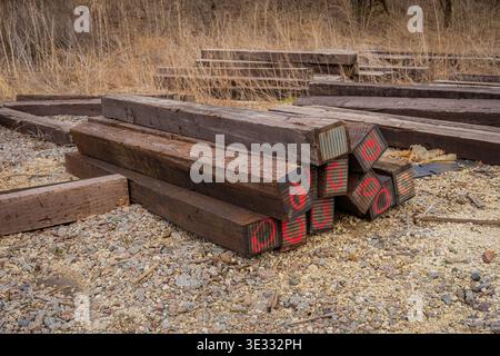 Stacks of weathered wooden railroad ties with red painted markings on gravel in rural storage yard Stock Photo