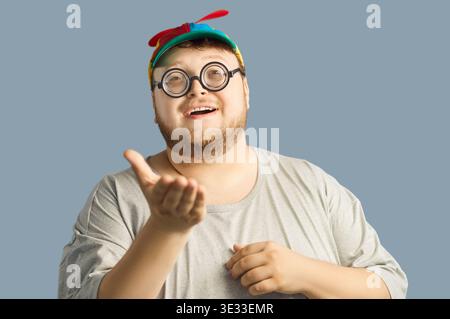 Smiling chubby man in propeller beanie and glasses, inviting gesture, studio Stock Photo