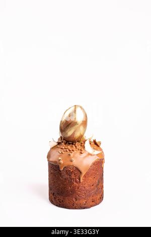 Traditional Easter kulich with chocolate icing, adorned with a gold egg and decorative elements: coconut flakes and gold spheres. Shot on white backgr Stock Photo