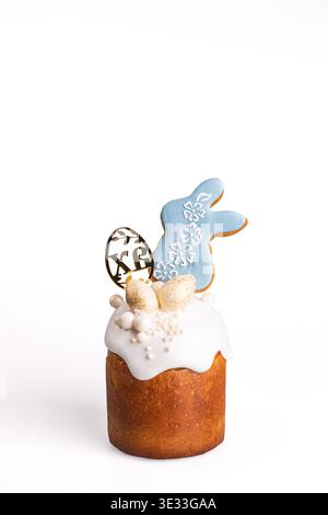 Traditional Easter kulich with golden-brown crust, light blue icing drip, white fondant bunny decorated with silver dragees and pearls, creamy flowers Stock Photo