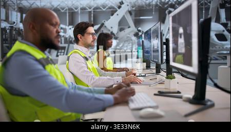 Diverse Team Of Engineers And Technicians Using Computers Designing Cars In An Automotive Factory Assembly Line Stock Photo