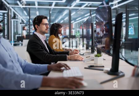 Diverse Group Of Financial Advisors Talking On Phones, Analyzing Trades. A Stockbroker Using A Computer Stock Photo