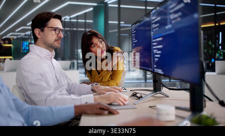 Diverse Tech Team Collaborates Closely Coding Software At Busy Office Desks. Several People, Including A Programmer Stock Photo