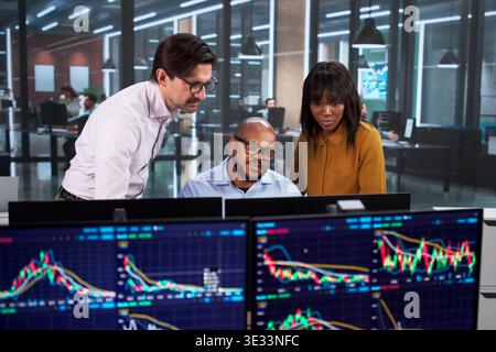 Diverse Team Of Workers Using Computers, Discussing Stock Charts, Planning Financial Strategies, Trading In The Market Stock Photo