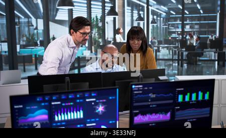 Diverse Team Of Financial Analysts Collaborates Using Computers And Data Screens. Several People, Including An Advisor Stock Photo