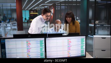 Young Analyst And Team Using Computers, Reviewing Data Spreadsheets, And Coding Reports In A Modern Office Stock Photo