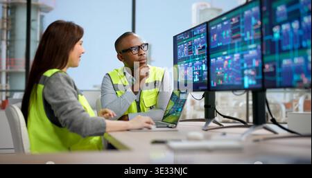 Young Woman And Man Monitoring Chemical Plant Production On Multiple Screens Stock Photo