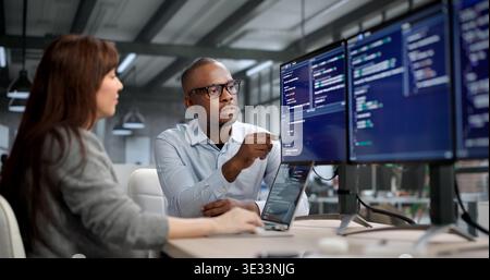 Female Software Developer Codes On Computer While A Manager Leads Training Stock Photo