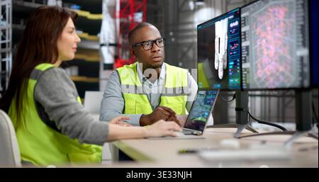 Two Engineers, A Man And Woman, Discuss Rocket Engine Designs On A Big Computer Screen Using 3D CAD Software Stock Photo