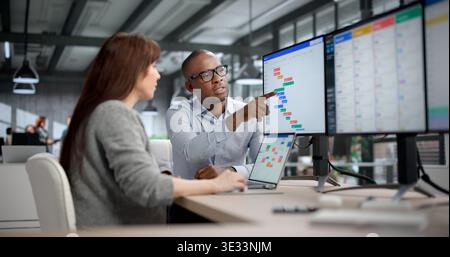 Young Woman And Man Coordinate Tasks Using Scheduling Software In Busy Office Setting. They Manage Calendars Stock Photo