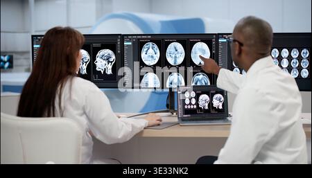 Two Medical Technicians Carefully Analyze Brain Scans On Computer, Collaborating In Clinic Stock Photo