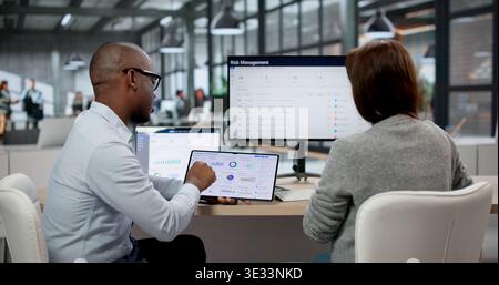 Two Young Professionals Using Multiple Screens To Monitor Data, Manage Business Risks, And Ensure Compliance Stock Photo