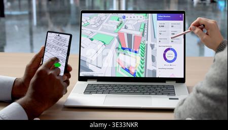 Two Engineers Discuss Site Plans Using Laptop And Smartphone For Mapping, Design, And Inspection Work Stock Photo