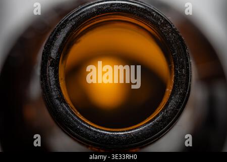 High detail macro close up of dark amber glass bottle opening with black rim and glowing interior Stock Photo