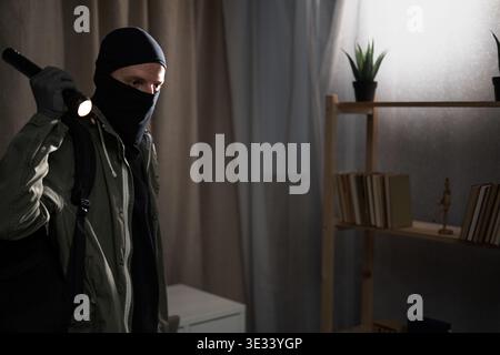 Burglar of Thief in black balaclava with flashlight inside of a house or office. Masked face. Copy space Stock Photo