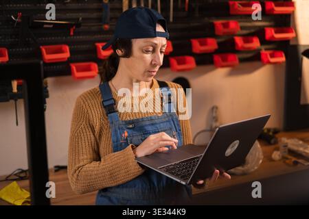 Creative woman managing small business online using laptop in restoration workshop. copy space Stock Photo