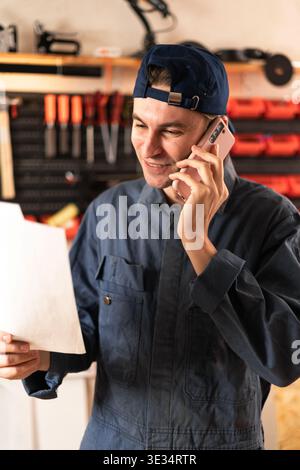 Repairman or mechanic examining paperwork and communicating using mobile phone working in garage. copy space Stock Photo