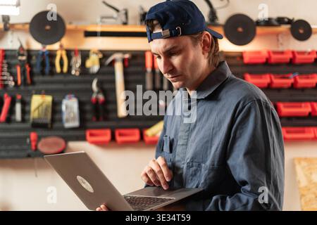 Portrait of confident small business owner craftsman using laptop at his workshop table. Professional male artisan in workwear looking at screen, doin Stock Photo
