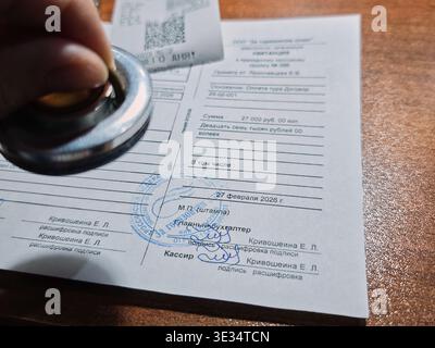 Kirov, Russia - February 27, 2026: A person is applying a stamp on a cash order document with details on a wooden surface. The date and amount are vis Stock Photo