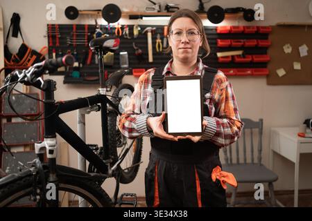Mechanic woman doing bike servicing showing white screen on tablet. online replacement bicycle parts. copy space Stock Photo