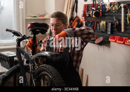 Professional female bike mechanic using screwdriver to fix bicycle seat preparing cycle for new season in workshop. copy space Stock Photo