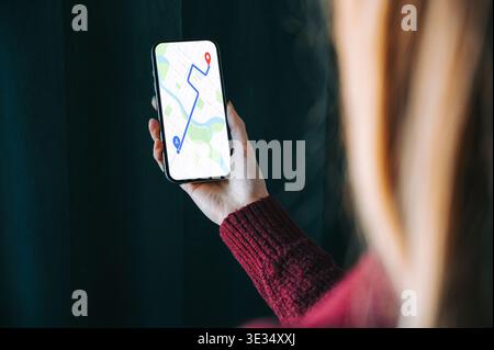 Over-the-shoulder view of a woman holding a smartphone with a GPS navigation map showing a route and destination pin. Perfect for concepts of travel, Stock Photo